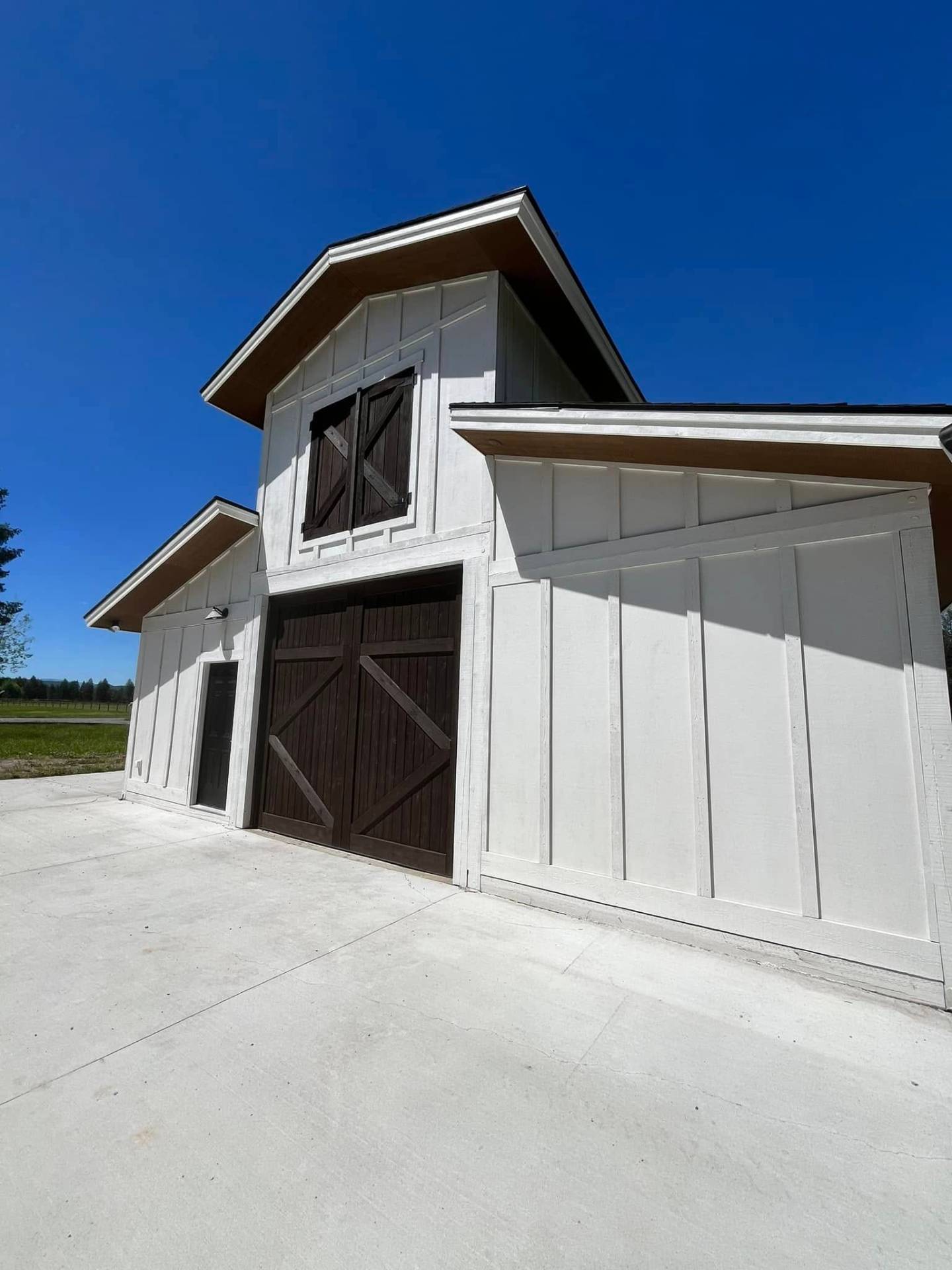 Board and batten barn exterior painted white with stained doors by Treeline Painting